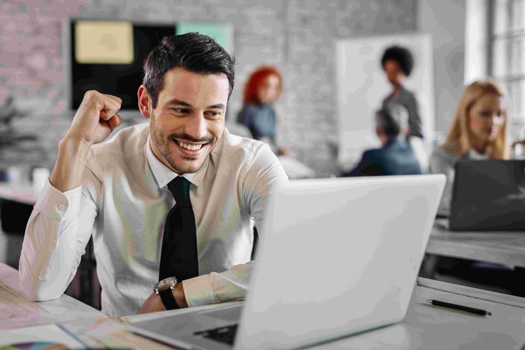 young-happy-businessman-using-computer-office-celebrating-good-news-there-are-people-background-compressed